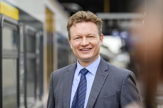 Karsten Schulz, der im Anzug lächelnd vor einem eurobahn Zug steht.  Im Hintergrund sieht man den Bahnsteig und einen weiß-gelben Zug .