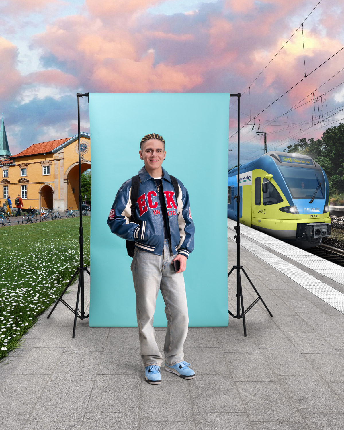Ein junger Mann in Collegejacke und heller Jeans steht vor einer türkisen Leinwand und lächelt in die Kamera. Links ist die Uni Osnabrück zu sehen mit Grünfläche zu sehen und rechts ein Zug der eurobahn. Die Szene spielt an einem Bahnsteig unter einem rosa-blau gefärbten Himmel.